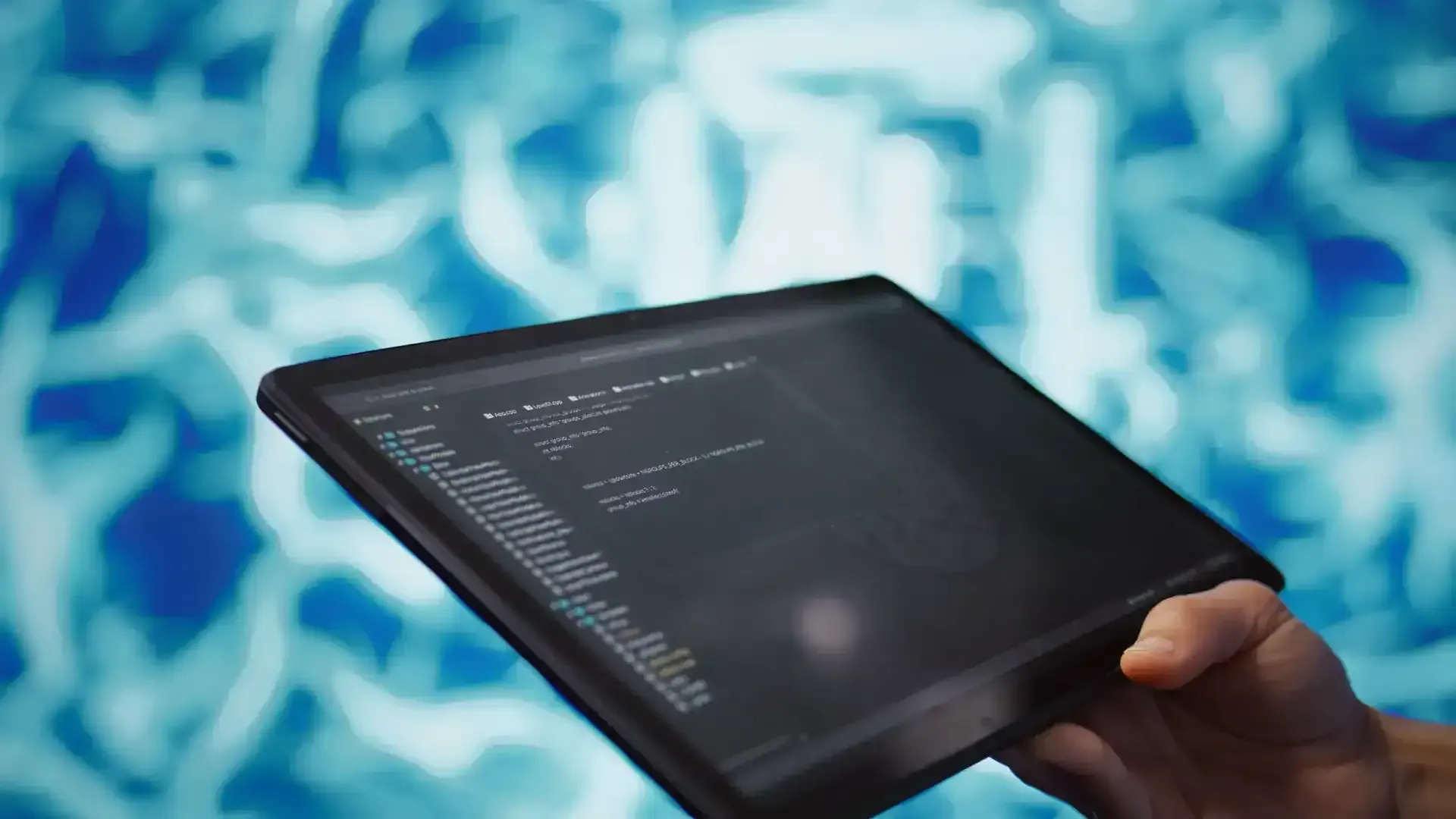 Mano che regge un tablet con un editor di codice aperto, davanti a uno sfondo astratto azzurro e bianco sfocato